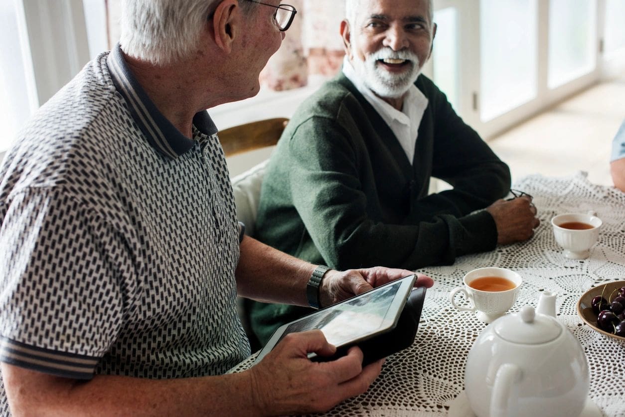 Two older men sitting at a table looking at an ipad.